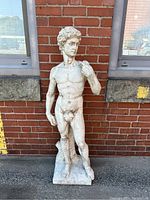 Full frontal view of the statue showing the figure of Adam standing against a brick wall.