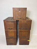 Seven oak filing drawers stacked in two columns with one on top, displayed against white wall.