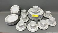 Photo showing the full set of plates, cups, and saucers arranged with visible floral and gold trim on white china.