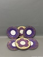 Eight Royal Worcester George Jones & Sons dinner plates arranged vertically and fanned out showing the purple luster and gold gilt decoration with white centers.