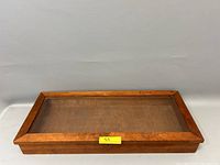 Front view of a closed vintage wooden display case with glass top showing the rectangular wooden frame and glass surface.