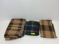 Three folded upholstery fabric pieces laid flat showing two plaid and one striped pattern.