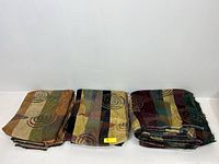 Three folded large vintage upholstery fabric pieces arranged side by side showing multi-colored vertical stripes and swirl patterns.