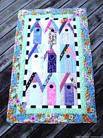 Front side of vintage handcrafted baby quilt showing colorful birdhouse applique design with flower and geometric patch borders