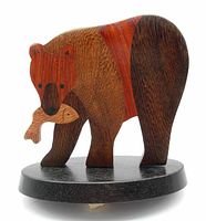 Front angled view of the wooden bear sculpture holding a fish in its mouth showing detailed parquetry woodwork and mounted on an oval base.