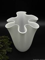 Front angled view of white amoeba-shaped glass vase with wavy rim and smooth glossy finish.