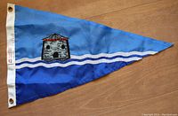 Photo of the triangular blue burgee flag with a Martello Tower emblem and white wavy lines on a wooden surface.