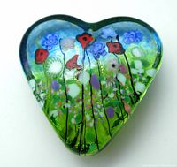Top view of heart-shaped glass paperweight showing colorful floral Murano elements inside green glass body.