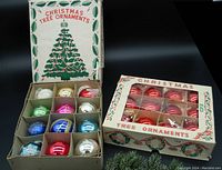Two boxes of vintage glass mercury Christmas tree balls in original boxes with festive graphics. One box contains assorted colors and designs, the other box contains uniform red balls.