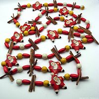 Full view of the garland showing wooden Santa star beads interspersed with round wooden beads in red, yellow, and white, and cinnamon stick bundles.