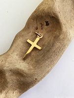 Photo showing the yellow gold cross pendant resting in a wooden bowl, highlighting its polished surface and classic cross shape.