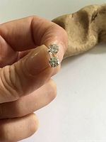 Close-up of both cubic zirconia solitaire stud earrings held in fingers, showing the stones and setting.