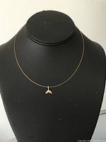 Whale tail pendant necklace displayed on a black presentation bust, showing the pendant centered on a thin gold chain.