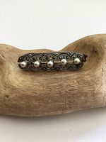 Front side view of antique silver bar brooch showing pearls and marcasite detailing on wooden display.