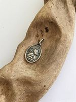 Photo of the oval-shaped sterling silver cupid pendant on a wooden surface showing front detail of raised cupid figure.