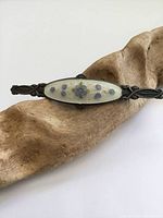 Top view of the antique sterling silver guilloche enamel flower brooch resting on a wood piece, showing detailed enamel flower design with minor tarnish on silver parts.