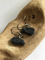 Pair of black argillite eagle carved earrings resting in a wooden bowl showing the detail and color of the stone with attached silver hooks.