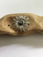 Front view of the Birks sterling silver flower brooch showing the marcasite decorated petals and central hematite or black diamond stone. The brooch is positioned on a piece of driftwood for display.