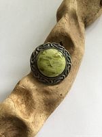 Front view of round Celtic sterling silver brooch with green agate placed on a textured wooden surface.