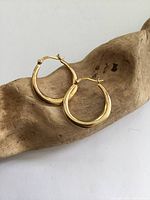 Pair of gilt sterling silver hoop earrings displayed on a wooden background, showing their round hoop shape and polished gold-toned surface.