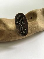 Oval silver-toned ring with an abstract modernist brutalist raised design on the face placed on a light wooden surface for detail and contrast.