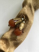 Pair of vintage earrings displayed on natural wood, showing amber teardrop shapes with yellow metal leaf frames and small pearls.