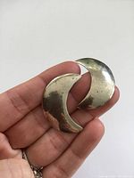 Two crescent-shaped sterling silver earrings held in hand with visible tarnish and surface marks.