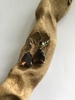Front angled view of earrings showing faceted tear drop quartz and smaller stone above, set in white metal, laid on textured wood