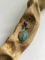 Snail pendant placed on a wooden surface showing the abalone shell inlay and silver head, close-up view.