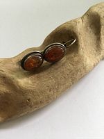 Pair of oval Baltic amber drop earrings in sterling silver bezels displayed on a wooden textured surface.