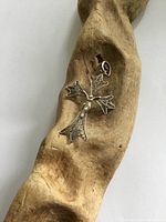 Filigree cross pendant placed on textured wood surface showing front detail and size.