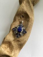 Sterling silver pendant with central oval lapis lazuli, surrounded by smaller round tanzanite stones, resting on a carved wooden display.