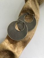 Front view of the silver hoop earrings on natural wood display, showing textured pattern and size.