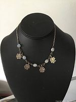 Full view of the sterling silver necklace displayed on a black stand showing five moonstone cabochons and four character charms.