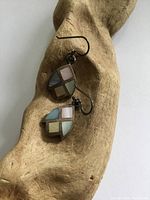 Pair of tulip-shaped sterling silver earrings with multi-colored mother of pearl inlays on a wooden background.