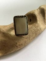 Rectangular mother of pearl ring on wood background, showing tarnish and surface wear.