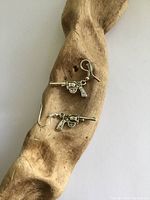 Two sterling silver revolver dangle earrings displayed on a piece of wood background. The earrings have detailed revolver shapes with hooks for ears.