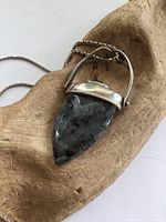 Close-up photo of the pendant showing agate stone and sterling silver setting on wooden background.