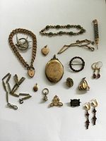 Overhead shot of all items laid out on white background: chains, lockets, brooches, bracelets, earrings, pendants and pencil