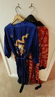 Two Chinese kimono robes on hangers, blue with dragon design and red with gold pattern.