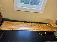 Full view of wooden toboggan laid flat on table, showing construction and rope details.