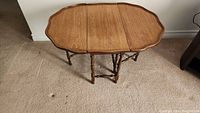 Full view of the antique walnut drop leaf coffee table showing the open oval top with scalloped edges and turned spindle legs.