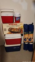 Photo showing all items in the lot – coolers, box for Tefal indoor barbecue, water jug, and two folded chairs in cases.