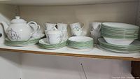 Full view of dishware set on shelf including teapot, cups, plates, sugar bowl, and bowls