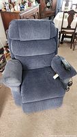 Front view of the blue upholstered lift chair in room setting showing cushions and remote control on armrest.