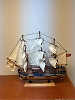 Full frontal view of the wooden H.M.S Endeavour model ship standing on a wooden base with three masts and white cloth sails.