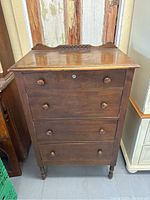 Full front view of tall four-drawer highboy with carved top gallery and round wooden knobs