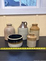 Full view showing all five jugs and crocks arranged in a row with measuring tape front for scale.