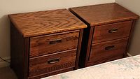 Two oak nightstands placed side by side against a wall, each with two drawers and metal handles, showing overall condition and structure.
