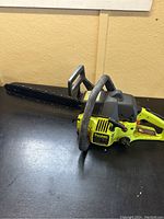 Full side view of the Poulan 2150 gas chainsaw placed on a black surface, showing the yellow and black housing and the 16 inch blade with chain attached.